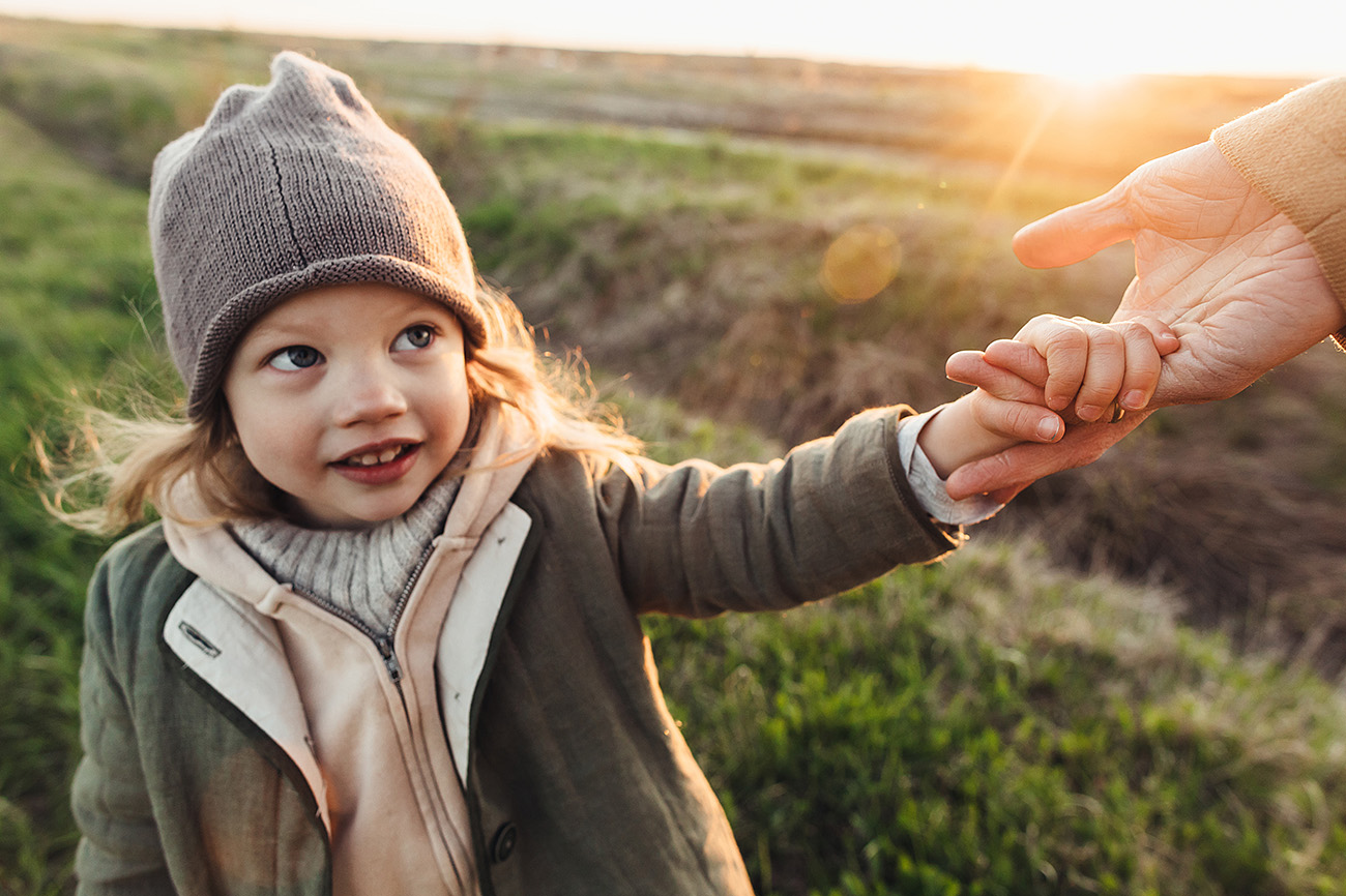 A young girl with a coat and hat takes the hand of an adult woman outside